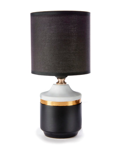 A black fabric-shaded table lamp with a white base and a gold-colored band