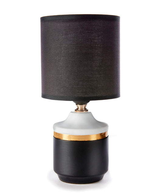 A black fabric-shaded table lamp with a white base and a gold-colored band