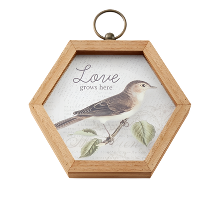 Hexagonal wooden frame with a bird illustration and 'Love grows here' text on a white background
