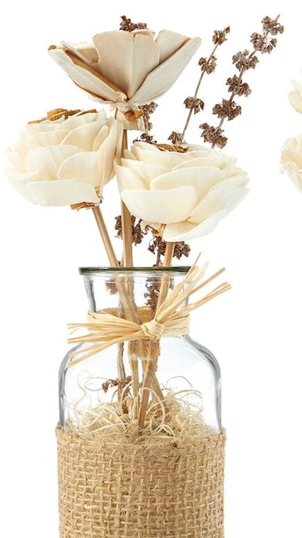 A clear glass jar containing an arrangement of natural dried flowers, tied with a rustic jute ribbon and adorned with bamboo sticks, cocoa fiber, shola flowers, wheat, palang, and teesi grass.